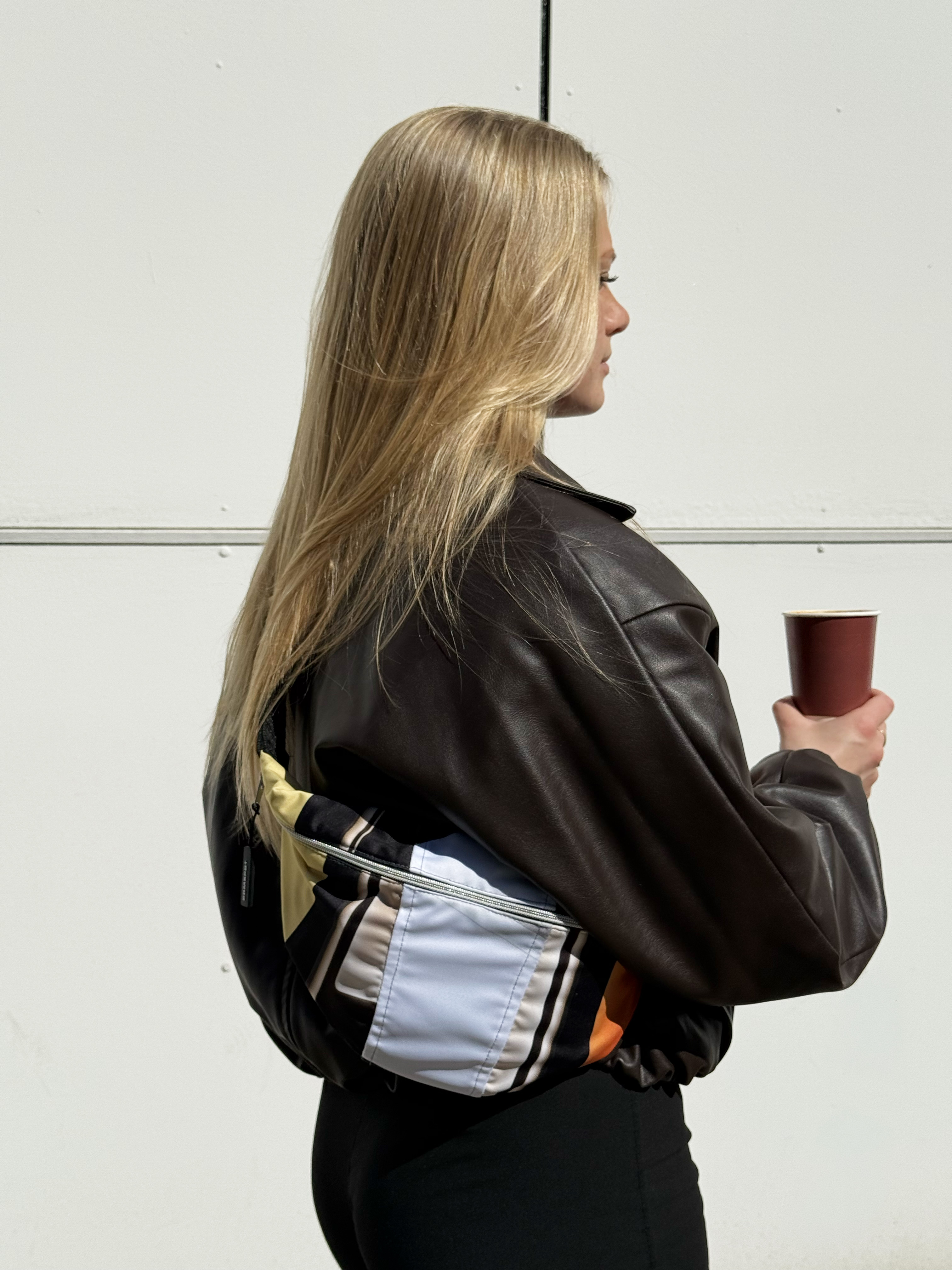 Model trägt große dunkle COMSPOT Upcycling Tasche vor Hauseingang